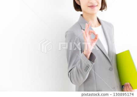 A middle-aged female business woman in a gray suit holding a file and making a circle sign A middle-aged female business woman in a gray suit holding a file and making a circle sign 130895174