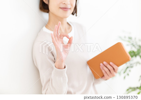 A middle-aged woman in casual clothes making a circle sign while holding a long wallet 130895370