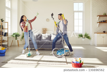 Funny couple cleaning home together having fun, dancing at home while housekeeping work 130896562