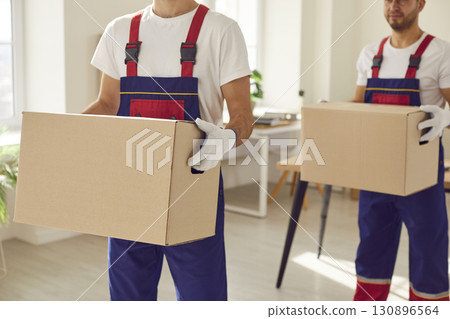 Two workers from a commercial moving service are carrying packed up cardboard boxes 130896564