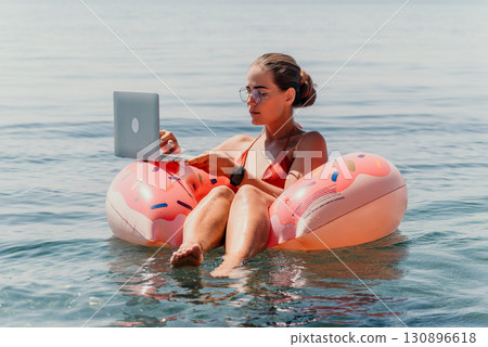 Woman Laptop Beach Working on Laptop While Relaxing on a Flamingo Float Woman Laptop Beach Working on Laptop While Relaxing on a Flamingo Float 130896618