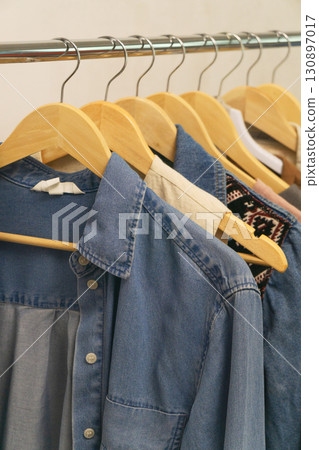Fashionable upcycled second-hand denim shirts hanging on wooden hangers in a trendy boutique 130897017