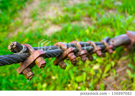 Thick wire rope fastening system with steel clamps and bolts on green natural background 130897082