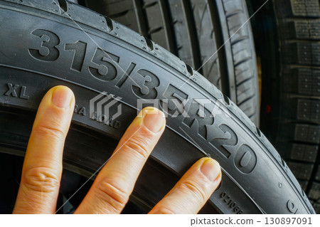 Close-up of car tire sidewall with size marking and hand pointing at tire size specifications Close-up of car tire sidewall with size marking and hand pointing at tire size specifications 130897091