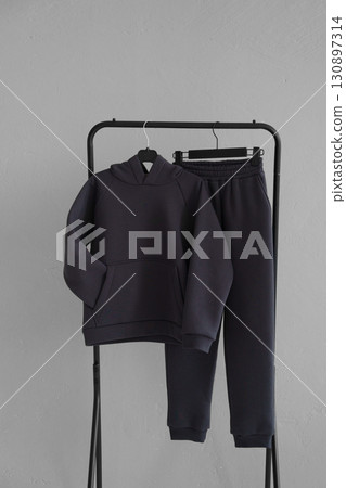 Fashionable warm gray cotton tracksuit on a hanger on a gray background. Fashionable warm gray cotton tracksuit on a hanger on a gray background. 130897314