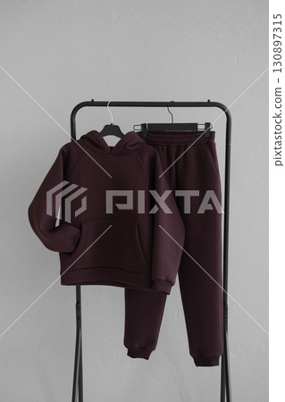 Fashionable warm brown cotton tracksuit on a hanger on a gray background. Fashionable warm brown cotton tracksuit on a hanger on a gray background. 130897315