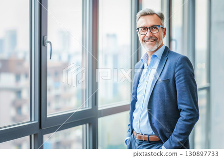Senior businessman with gray, standing by large office window overlooking the city, exuding professionalism and experience. Concept of leadership, executive success, and modern corporate culture 130897733