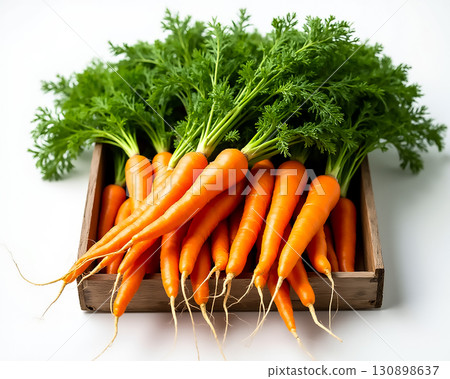 Freshly harvested carrots with green tops displayed in a rustic wooden crate on a light background 130898637