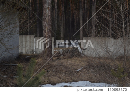 Abandoned broken fence leading into a dark pine forest. Mysterious atmosphere of decay, nature reclaiming space 130898870
