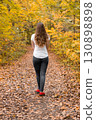 Young woman with long hair walking on autumn forest path covered with fallen leaves, symbol of calmness and nature 130898898