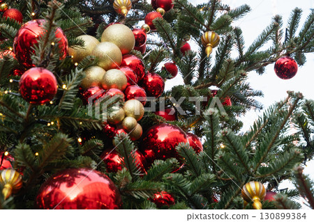 Festive background of natural Christmas tree with red and golden balls at city street. Xmas holiday spirit. Outdoors. Festive background of natural Christmas tree with red and golden balls at city street. Xmas holiday spirit. Outdoors. 130899384