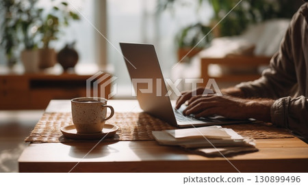 A person works on a laptop with a cup of coffee on a table near a comfy sofa 130899496