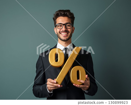 Businessman smiles while holding large golden percentage symbol in studio setting 130899923