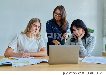 Two university student girls with female teacher mentor study while sitting at desk 130901128