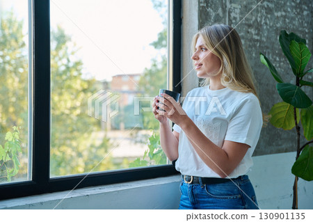 Young beautiful woman looking out the window with cup of coffee, profile view Young beautiful woman looking out the window with cup of coffee, profile view 130901135