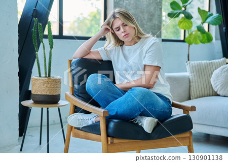 Unhappy upset tired young woman sitting in chair at home Unhappy upset tired young woman sitting in chair at home 130901138