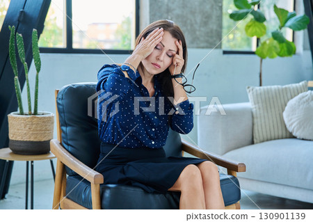 Mature sad woman experiencing stress, headache, mental pain, sitting in chair Mature sad woman experiencing stress, headache, mental pain, sitting in chair 130901139