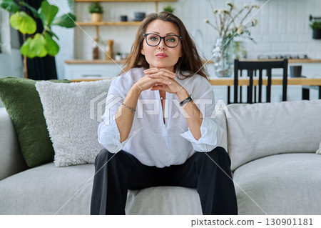 Successful beautiful mature woman looking at camera sitting at home on sofa Successful beautiful mature woman looking at camera sitting at home on sofa 130901181