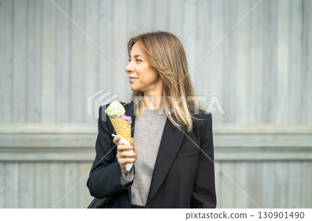 Delighted woman relaxing after work while eating frozen ice cream cone dessert, look away on streets 130901490