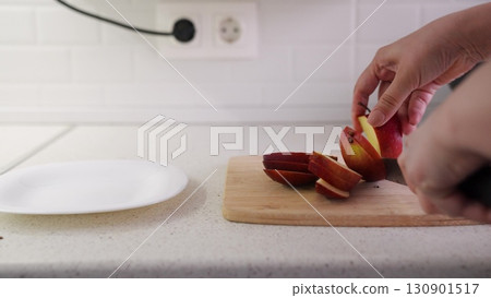 Kitchen counter view with apple, White plate and fruit prep, Fruit cutting with care, Red apple for healthy bite, Modern kitchen ambiance, Knife-hand coordination focus, Chopping apple for snack 130901517