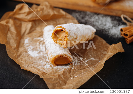 Caramel cream filled pastry rolls dusted with powdered sugar on parchment paper 130901587