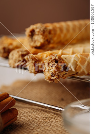 Close up of crispy wafer rolls with nut filling on rustic burlap and metal rack 130901597