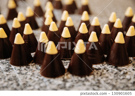 Chocolate cone candies with white tips arranged on granite surface in confectionery workshop 130901605