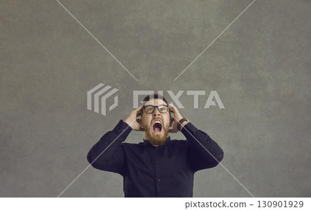Mad furious caucasian man shouting aggressively holding his head on a gray background. Mad furious caucasian man shouting aggressively holding his head on a gray background. 130901929