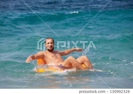 Happy kids have fun in sea surf on beach. Joyful couple of children on inflatable ring ride on breaking wave. Travel lifestyle, swimming activities in family summer camp. Vacations on tropical island 130902326