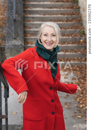Gray-haired woman of sixty years old in a red coat and a green scarf  130902376