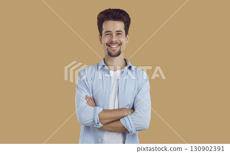 Portrait of smiling young man with neatly shaved beard and mustache, dressed in white T-shirt and blue shirt, confidently looking straight, arms crossed on his chest. 130902391