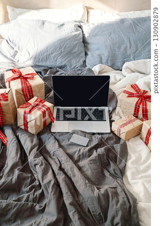 Laptop, credit card, and many gift boxes on cozy bed. Laptop, credit card, and many gift boxes on cozy bed. 130902879
