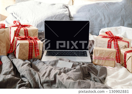 Laptop with blank screen, credit card and wrapped gift boxes on casual bed. Online holiday shopping. Laptop with blank screen, credit card and wrapped gift boxes on casual bed. Online holiday shopping. 130902881