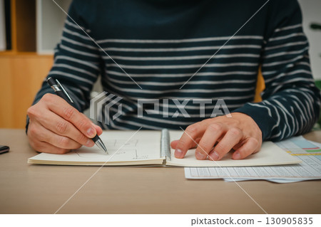 hand holding pen and wtiting notebook at home office 130905835