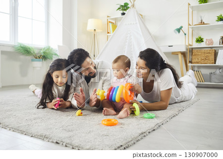 Happy father, mother small girl and her sister lying together on floor playing with colorful pyramid Happy father, mother small girl and her sister lying together on floor playing with colorful pyramid 130907000