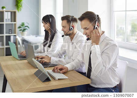 Customer care operators with headsets handling calls on laptops in airy office Customer care operators with headsets handling calls on laptops in airy office 130907007