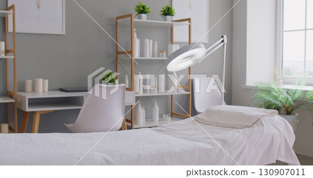 Bright modern spa treatment room with massage table, magnifying lamp and shelves Bright modern spa treatment room with massage table, magnifying lamp and shelves 130907011