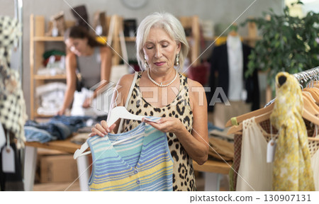 Attentive mature woman choosing something for summer in clothing store Attentive mature woman choosing something for summer in clothing store 130907131