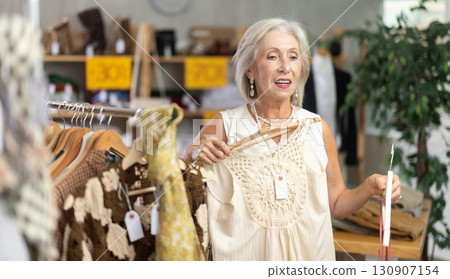 Positive mature woman choosing something for summer in clothing store 130907154