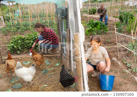 Mom and her daughter feed chickens in chicken coop in backyard of country house Mom and her daughter feed chickens in chicken coop in backyard of country house 130907160