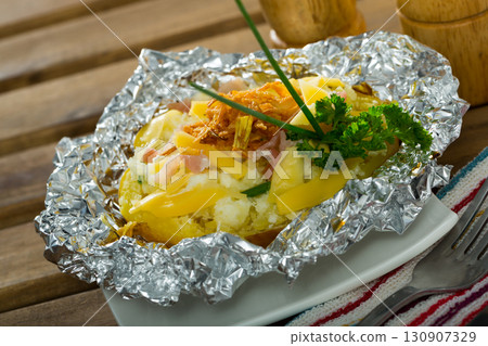 Baked in foil potatoes with filling of bacon, cheese and fried onion Baked in foil potatoes with filling of bacon, cheese and fried onion 130907329