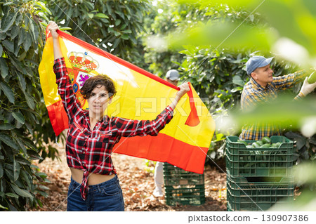 Happy young Latin female waving Spanish flag during avocado harvesting season on farm Happy young Latin female waving Spanish flag during avocado harvesting season on farm 130907386
