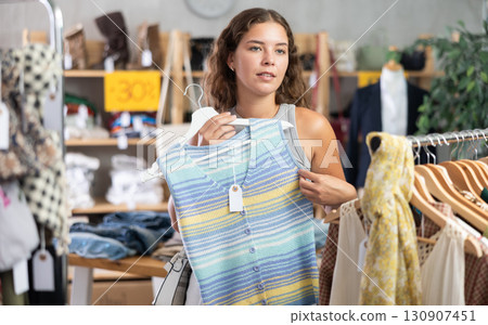 Positive young woman choosing something for summer in clothing store 130907451