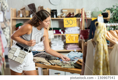 Positive young woman choosing trousers in clothing store 130907541
