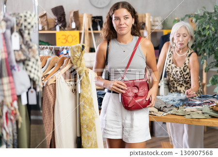 Happy young woman choosing handbag in clothing store 130907568