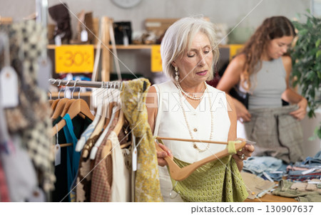 Attentive mature woman choosing something for summer in clothing store Attentive mature woman choosing something for summer in clothing store 130907637