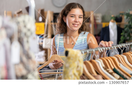 Positive young woman choosing something for summer in clothing store Positive young woman choosing something for summer in clothing store 130907657