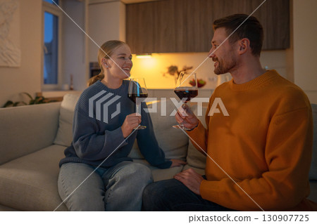 Smiling happy couple toasting with wine glasses, relaxing on sofa in romantic evening at home Smiling happy couple toasting with wine glasses, relaxing on sofa in romantic evening at home 130907725