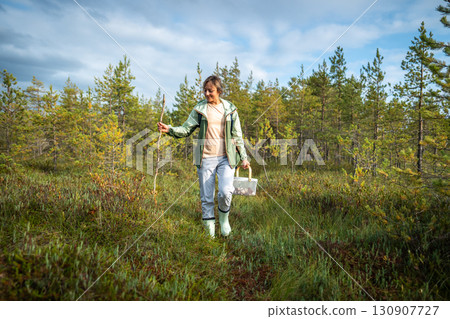 Happy woman walking with stick on raised peat bog in forest foraging for mushrooms alone in autumn Happy woman walking with stick on raised peat bog in forest foraging for mushrooms alone in autumn 130907727