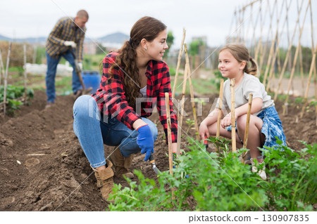 Daughter helps mother clean weeds in farmer garden beds Daughter helps mother clean weeds in farmer garden beds 130907835